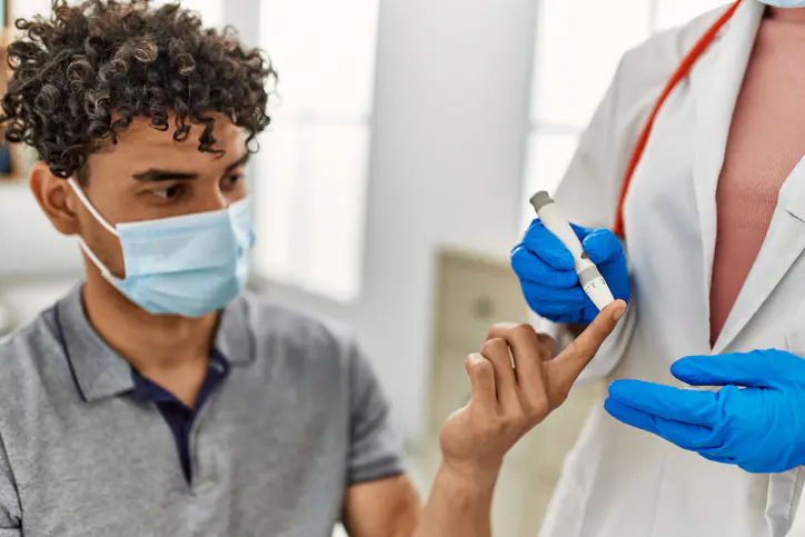 Young latin doctor woman wearing medical mask measuring gluscose at examination room.